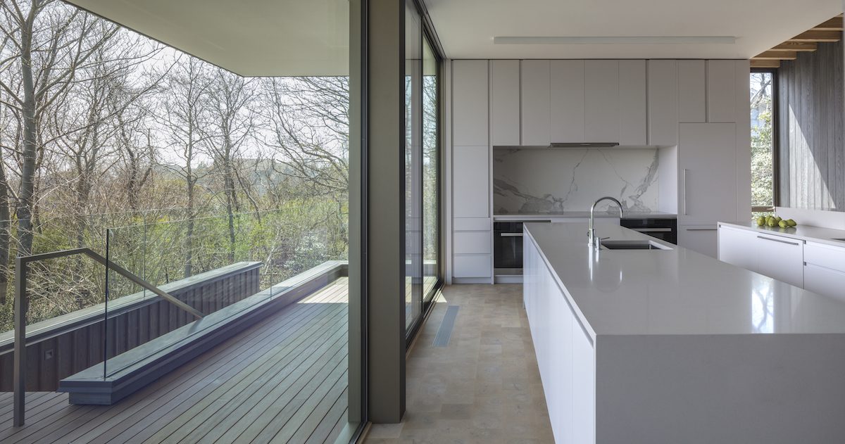 A modern kitchen with large windows overlooking a wooded area.