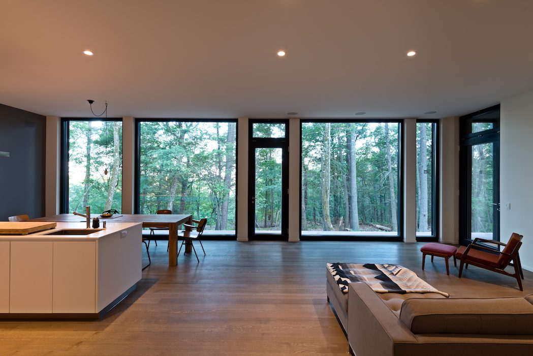 A living room with large windows overlooking a wooded area.