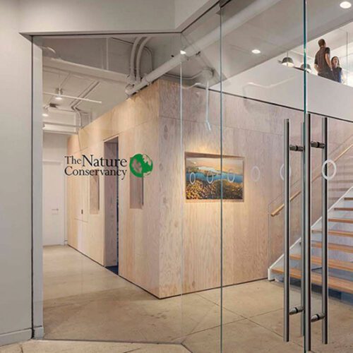 A glass office with stairs and a painting on the wall.