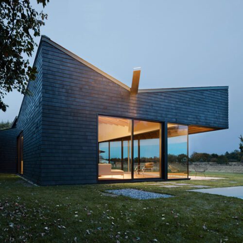 A modern house in the middle of a field at dusk.