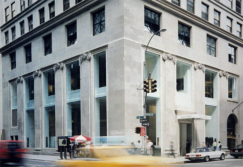 A yellow car drives past a building on a street.