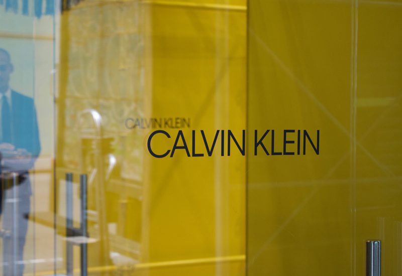 A man in a suit is standing in front of a sign that says calvin klein.