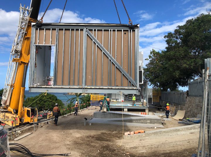 A crane lifts a metal building onto a construction site.
