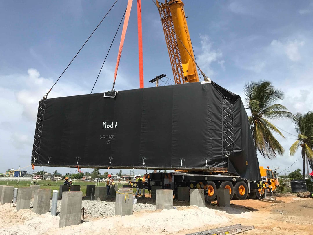 A crane lifts a large black box onto a construction site.
