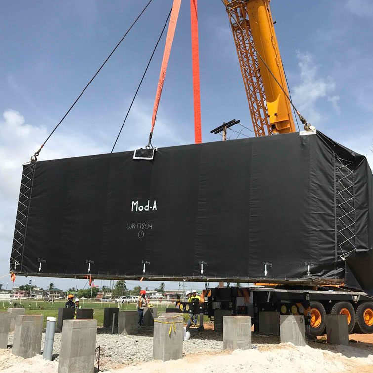 A crane lifts a large black box onto a construction site.