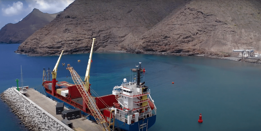 A large ship docked in the ocean near a mountain.