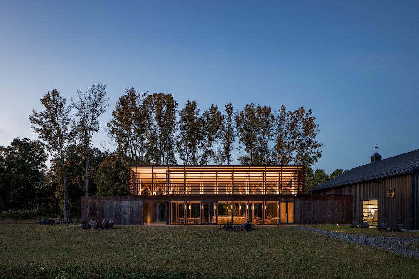 A modern farmhouse in the middle of a field at dusk.