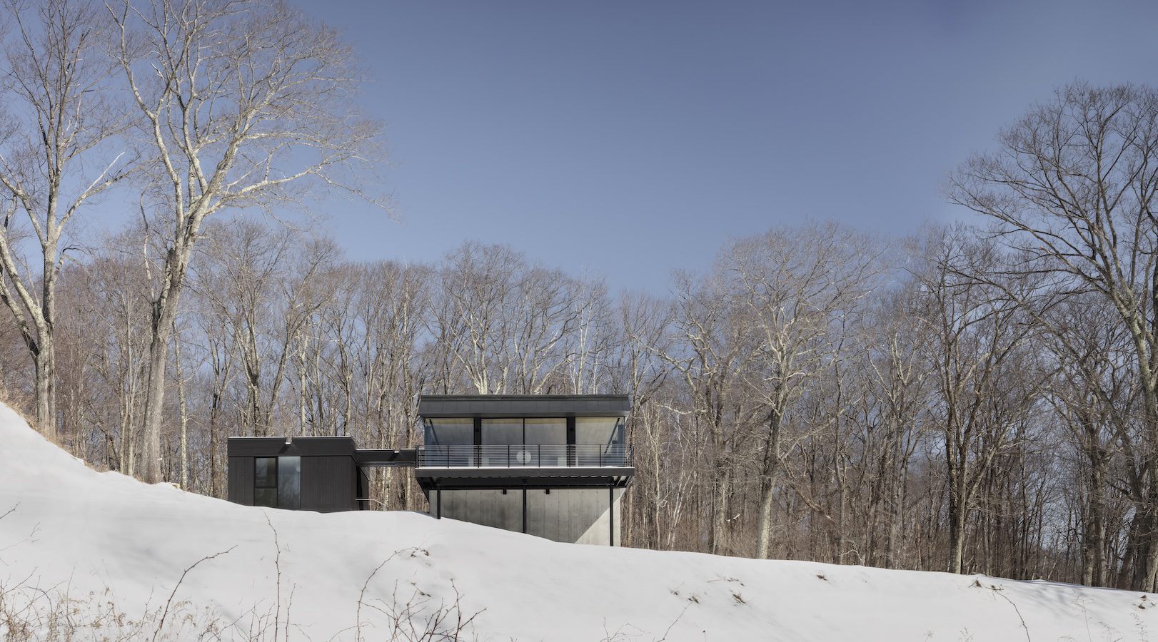 A modern residential house sits on top of a snowy hill, showcasing innovative structural design.